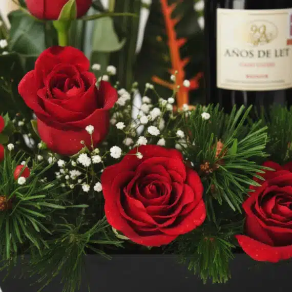 Primer plano extremo de arreglo floral CINZIA con 12 rosas rojas, gotas de rocío, follaje verde y botella de vino tinto.