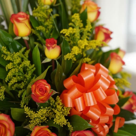 Primer plano extremo de un arreglo floral exótico con rosas bicolores (naranja y amarillo), follaje verde intenso y pequeñas