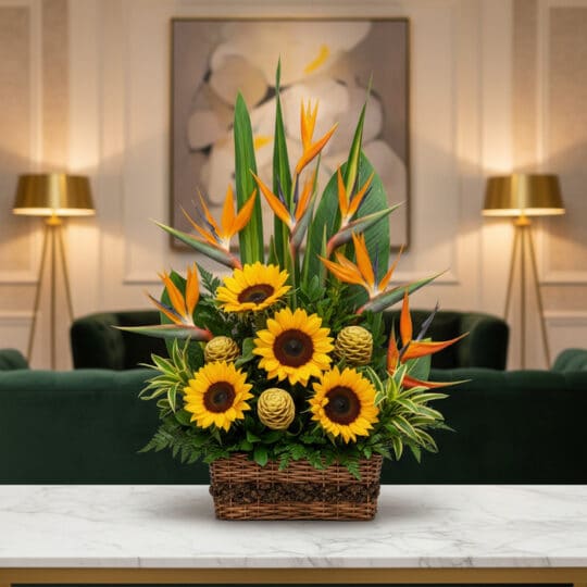 Arreglo floral Fantasía con girasoles vibrantes, exóticas aves del paraíso y detalles verdes en cesta de mimbre, sobre mesa d
