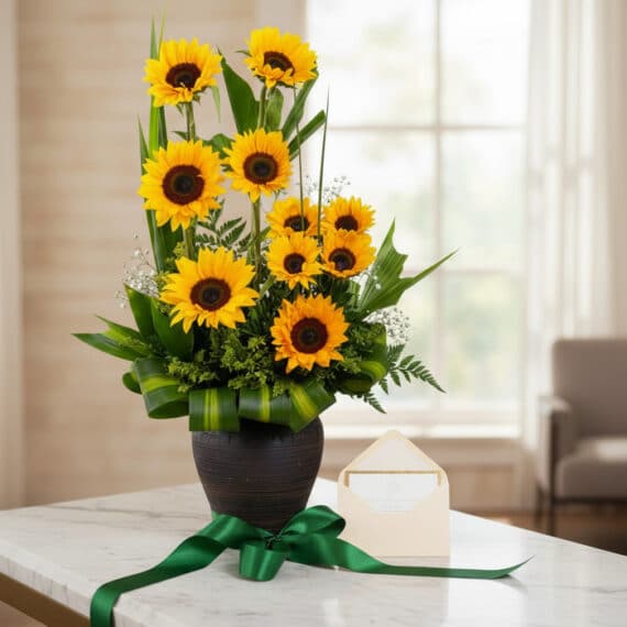 Arreglo floral GIULIANA con girasoles radiantes en jarrón oscuro, sobre mármol, con tarjeta de regalo y cinta verde satinada,