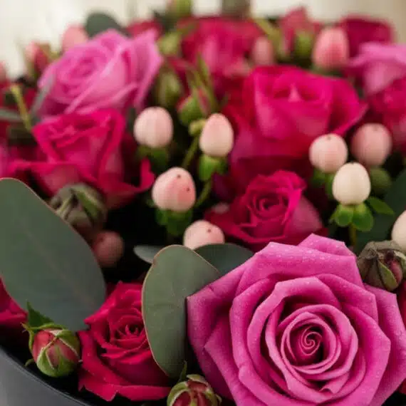 Primer plano extremo de Arreglo Floral LILIAN con rosas lila y rojas, capullos y hojas verdes, gotas de rocío, textura hiperr