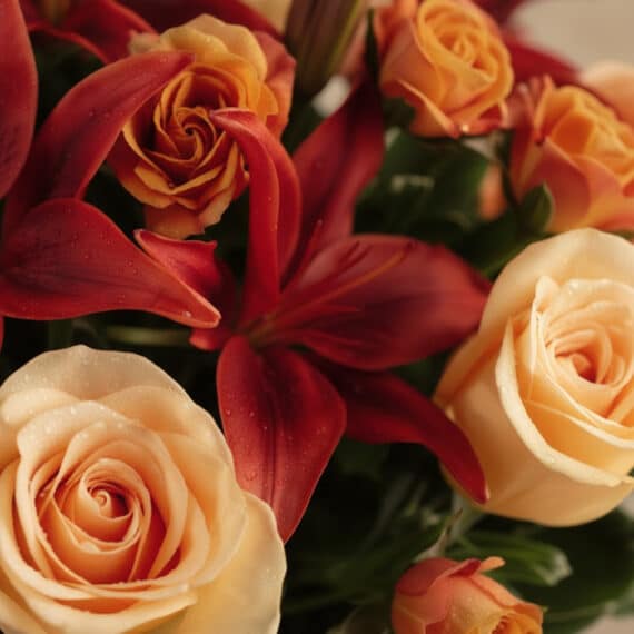 Primer plano extremo de un arreglo floral ALESSANDRA con rosas naranjas y lirios rojos, mostrando texturas hiperrealistas y g