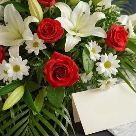 Arreglo fúnebre cubre caja Paraíso con rosas rojas, lirios blancos y margaritas, con rocío sutil y follaje verde, vista macro