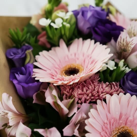 Primer plano extremo de un bouquet floral CARINA con gerberas rosadas, astromelias y lisianthus morados, destacando texturas