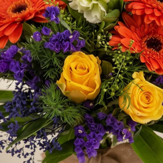 Primer plano extremo de un Bouquet Floral SABRINA con rosas amarillas, gerberas naranjas y flores moradas, mostrando gotas de