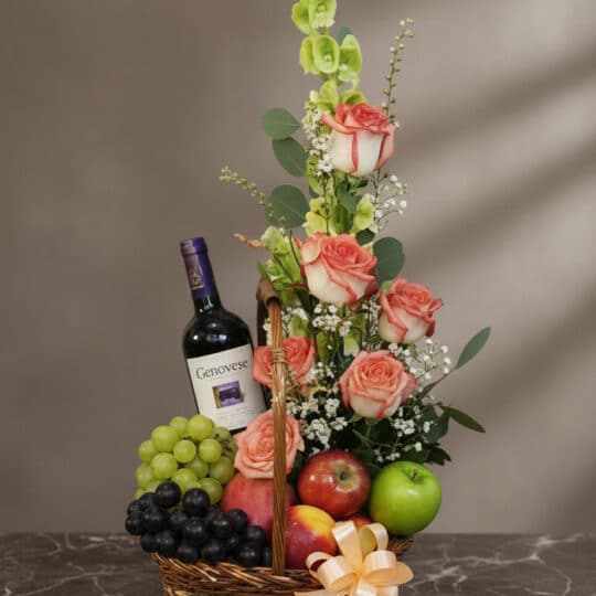 Cesta gourmet CAPRICE con rosas frescas, uvas verdes y negras, manzanas rojas y verdes, duraznos y una botella de vino tinto