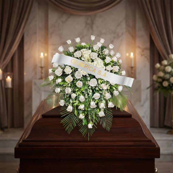 Cubre Caja Fúnebre Bernardita: Un Manto de Paz y Amor Cubre caja fúnebre Bernardita con rosas blancas y follaje verde sobre un ataúd de madera oscura, en un entorno elegante y sol